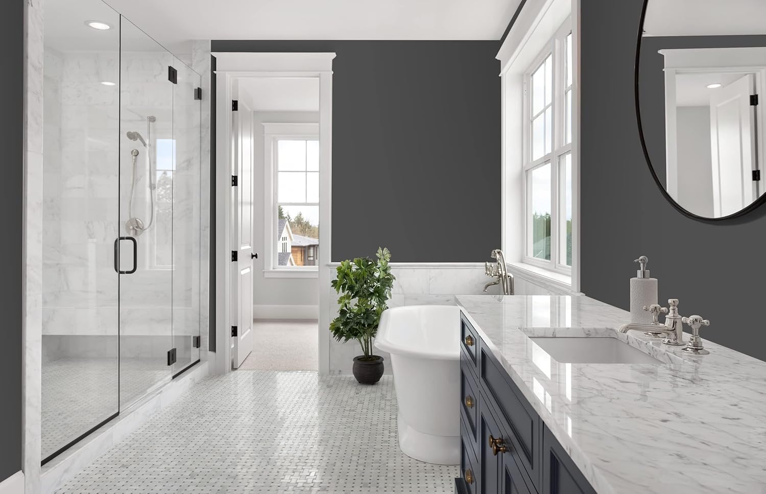 Modern bathroom with gray walls painted using a paint and primer in one, marble countertops, a freestanding bathtub, glass shower, and blue vanity. Large windows bring in natural light, and a green potted plant sits by the tub.