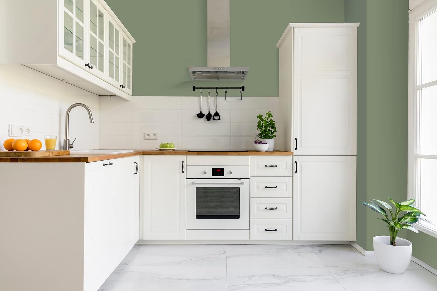 A modern kitchen featuring white cabinetry with a wooden countertop and a built-in oven. A potted plant sits next to the window, and oranges are displayed in a bowl on the countertop, creating a bright and inviting atmosphere.