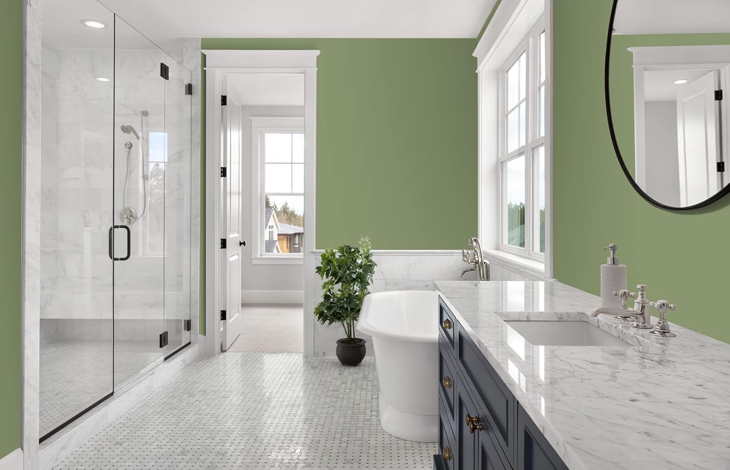 A spacious bathroom featuring a walk-in shower with glass doors, a freestanding bathtub, and a double-sink vanity. The walls are painted a soft green, complemented by marble countertops and a patterned tile floor. Natural light floods the room through large windows.