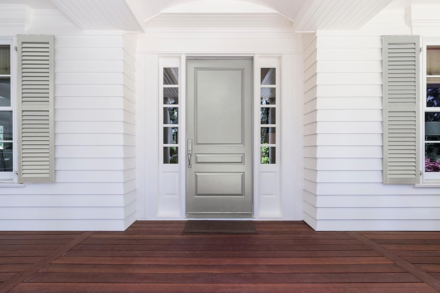 A modern entrance featuring a gray front door flanked by narrow windows, set against a backdrop of white siding and light gray shutters, with a wooden porch decked in rich brown hues.