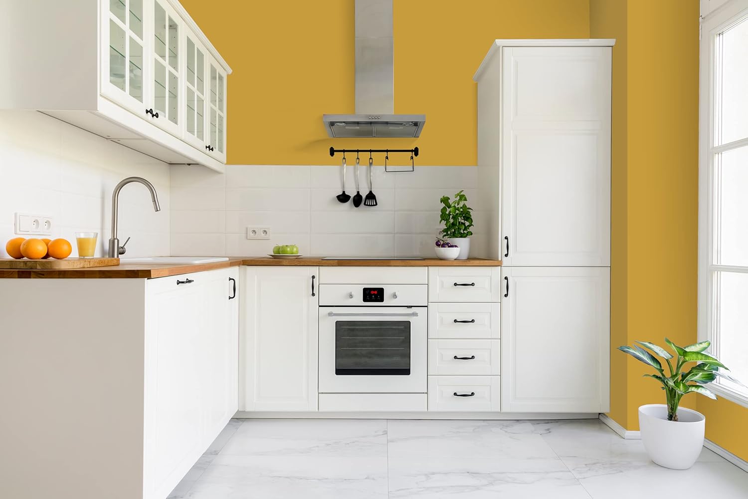 A modern kitchen with white cabinets and wooden countertops, a built-in oven, a range hood, and a sink. The yellow walls feature smooth coverage from thick satin finish paint, while plants and oranges add fresh decoration as natural light streams in.