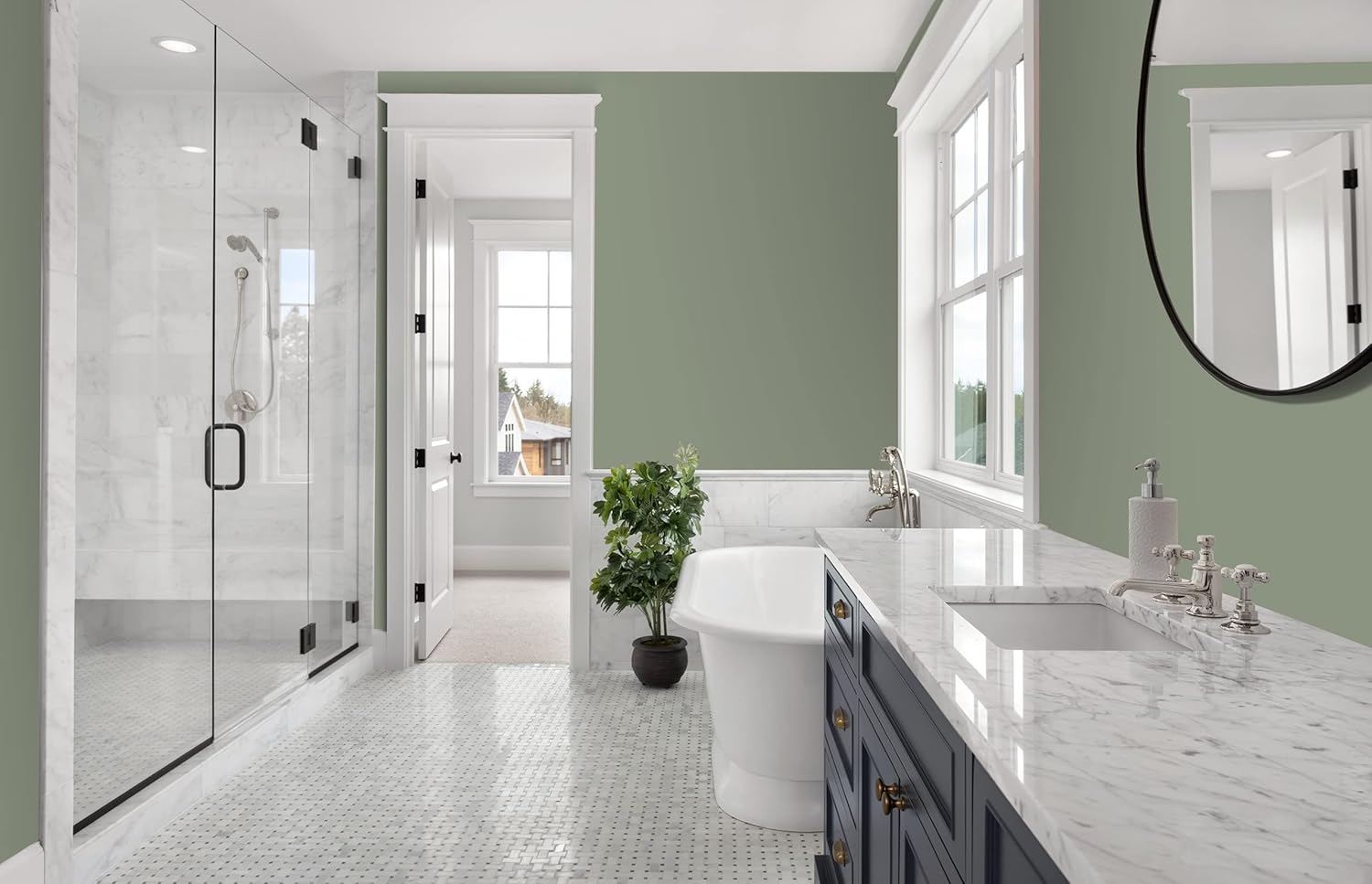 A contemporary bathroom featuring a glass shower enclosure, a freestanding white bathtub, and a double vanity with a marble countertop. The walls are painted a soft green, adding a calming touch. Natural light floods through large windows.