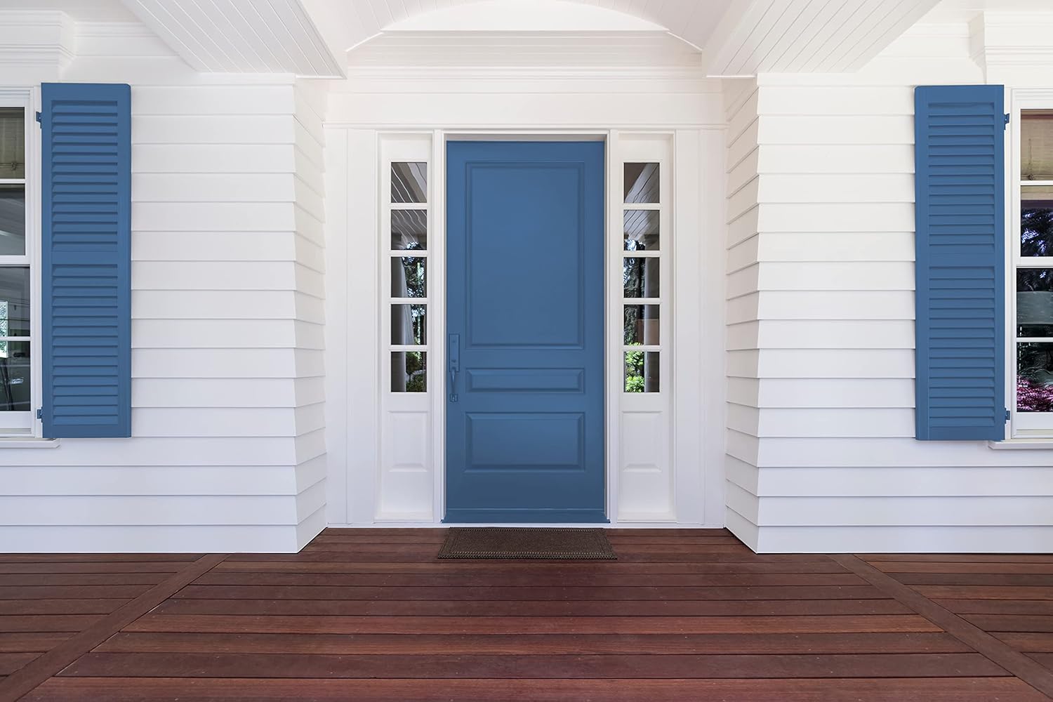 Front door of a white house with horizontal siding, blue shutters, and a blue door in the center finished with thick satin finish paint, flanked by glass side panels; wooden porch flooring in the foreground.
