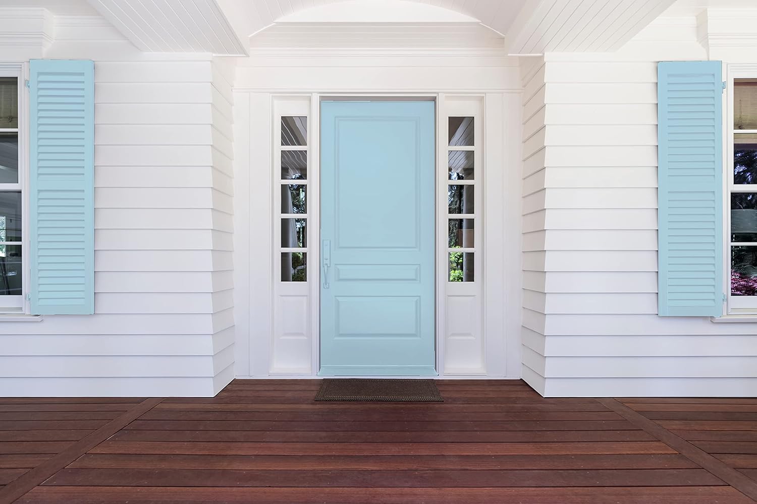 A light blue front door with matching shutters on a white-paneled house, flanked by windows and a wooden porch, stands out beautifully thanks to premium paint, with a doormat in front of the entrance.