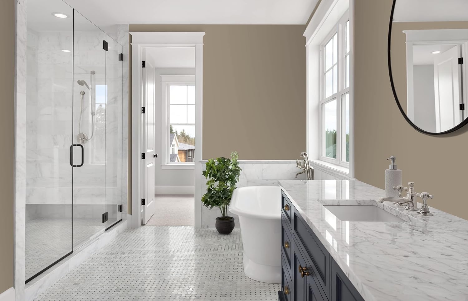 Modern bathroom with a glass shower, freestanding bathtub, marble countertop, blue vanity coated in thick satin finish paint for smooth coverage, large mirror, potted plant, tile floor, and two large windows letting in natural light.