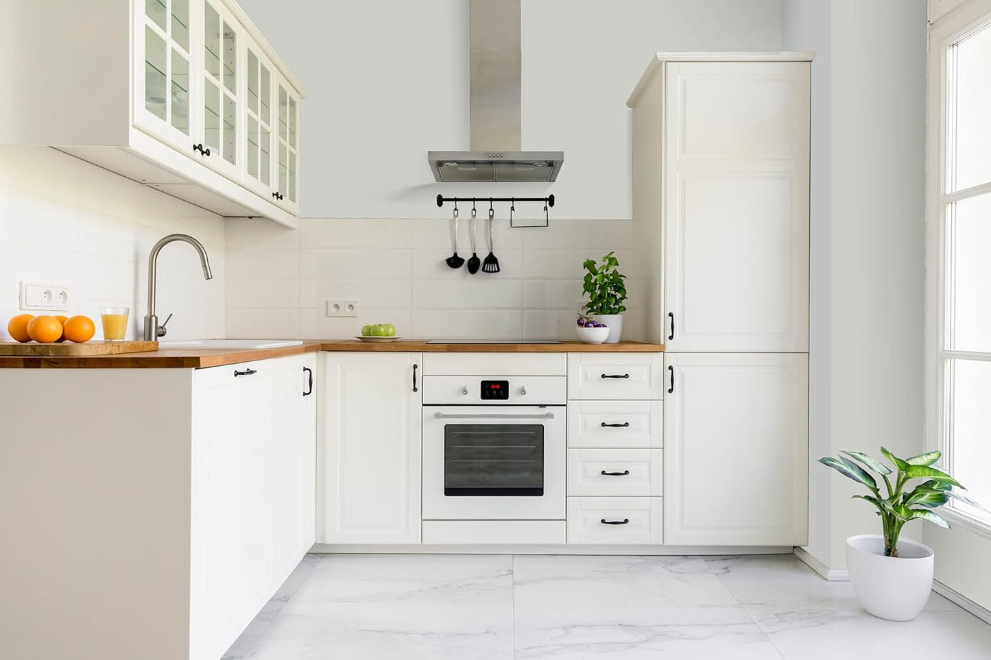 Modern white kitchen with wooden countertops, a built-in oven, and white cabinets finished with premium interior paint. Sunlight streams in through the window, highlighting green apples and a potted plant on the counter.