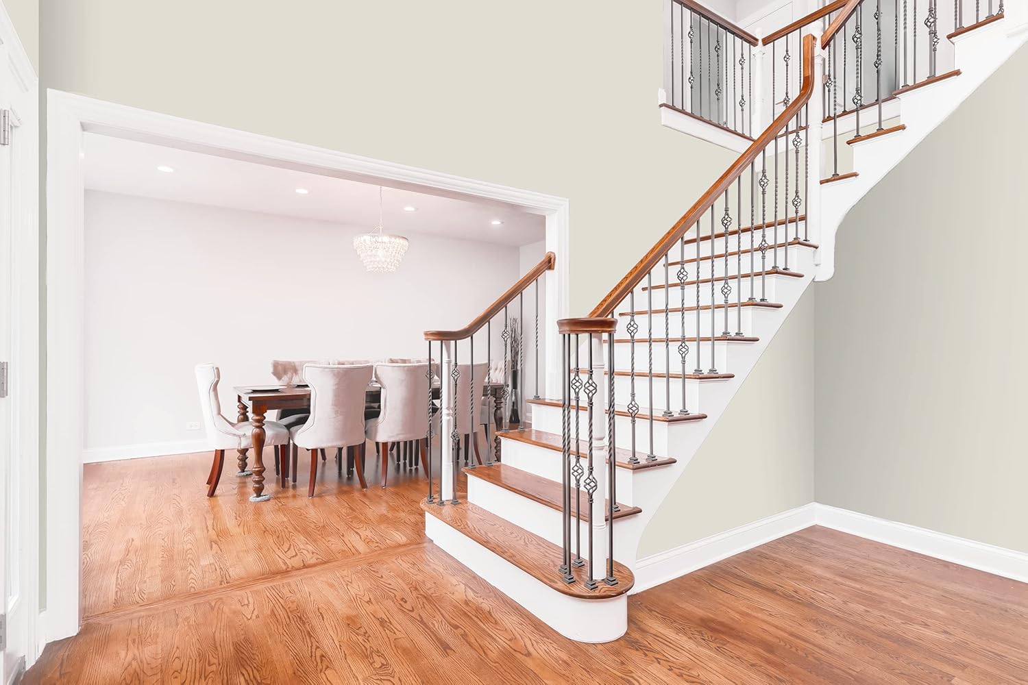 A bright, modern interior with wooden floors, a staircase with wood and metal railings, and an open dining area featuring a large table with upholstered chairs and a chandelier—all enhanced by best DIY home paint in a satin finish.