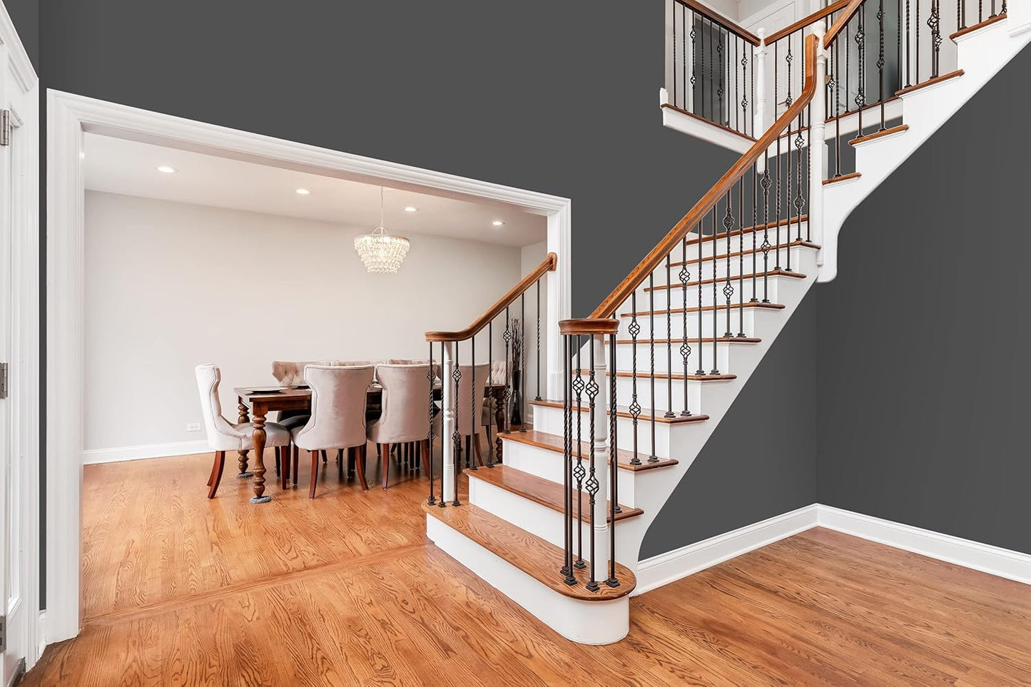 Elegant entryway with wooden staircase featuring white risers and black iron balusters. Adjacent open dining area with chandelier, wooden table, and upholstered chairs. Walls painted in the best DIY home paint with a satin finish for a timeless look.