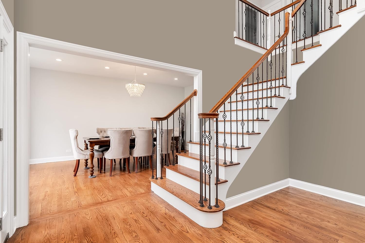 A modern dining room with a wooden table, three chairs with gray cushions, and minimalist decor on a herringbone floor stands out against a taupe wall finished in thick satin finish paint for smooth coverage. A vase of dried flowers adds charm.