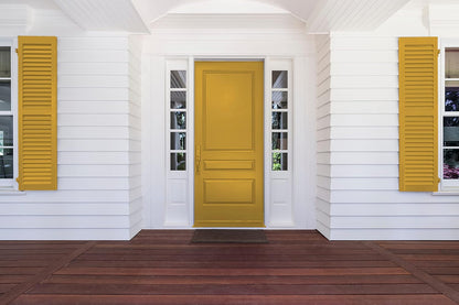 Front porch of a house with white siding, a large yellow front door coated in thick satin finish paint, yellow shutters on both sides, and dark brown wooden flooring. There are narrow windows flanking the door.