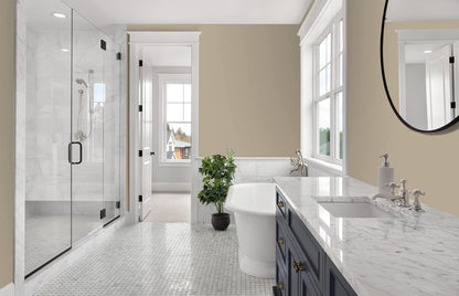 Modern bathroom with marble surfaces, glass shower, freestanding bathtub, navy vanity finished in premium interior paint, round mirror, and a potted plant near a window letting in natural light.
