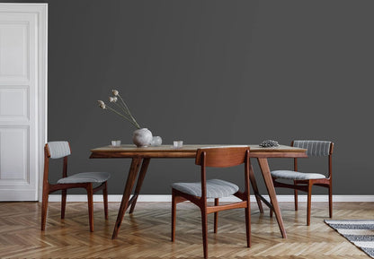 Minimalist dining room with a wooden table, three wooden chairs with gray cushions, and a gray vase with dried flowers. The dark gray wall is finished with the best DIY home paint for a flawless look in just one coat. Light herringbone floor and white door complete the space.
