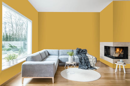 A modern living room with yellow walls painted in thick satin finish paint, a large window, a light gray sectional sofa, a round white rug, a small white table with a plant, and a corner fireplace with a burning fire.